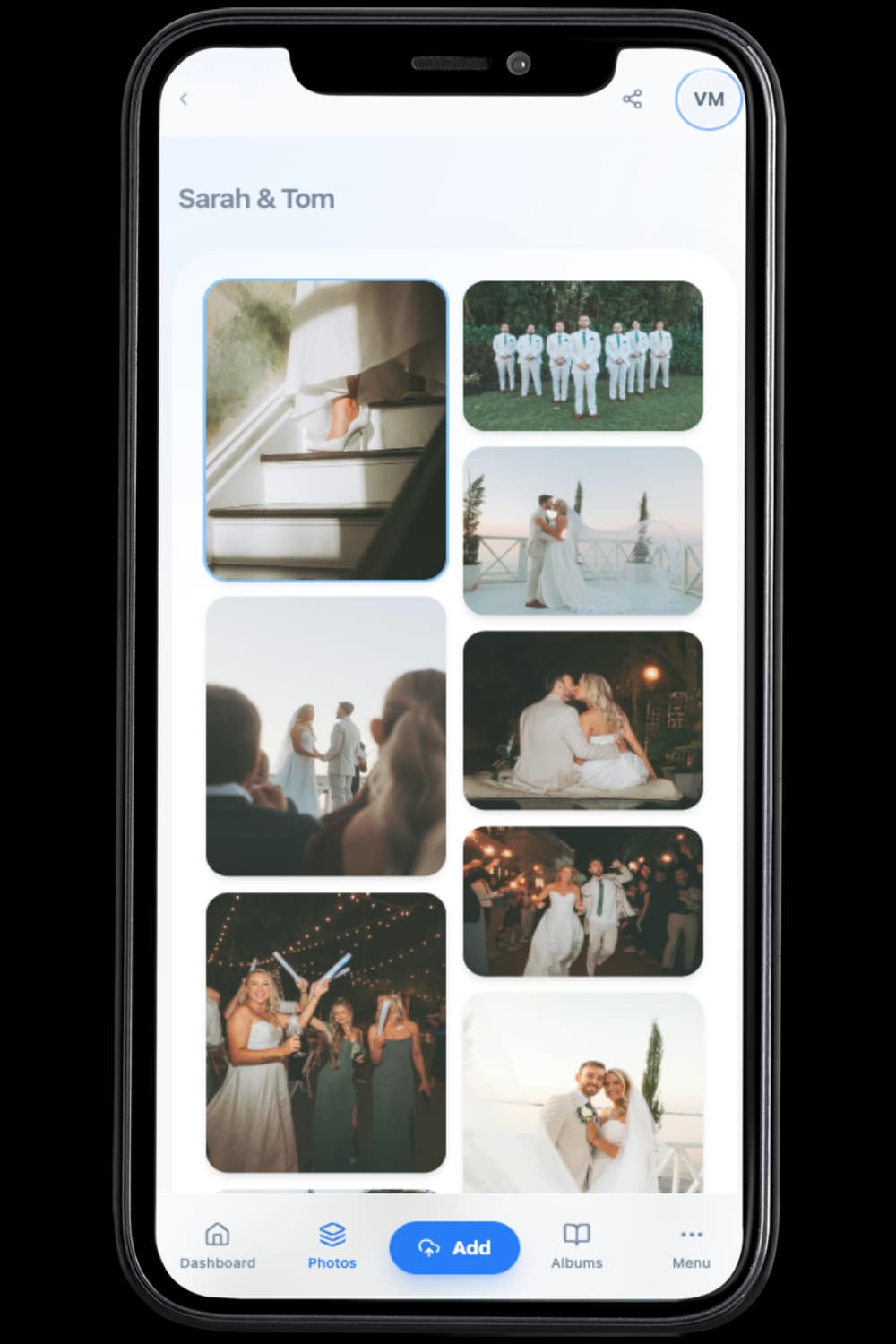 Happy wedding couple reviewing shared event photos on a tablet with guests enjoying the party in the background